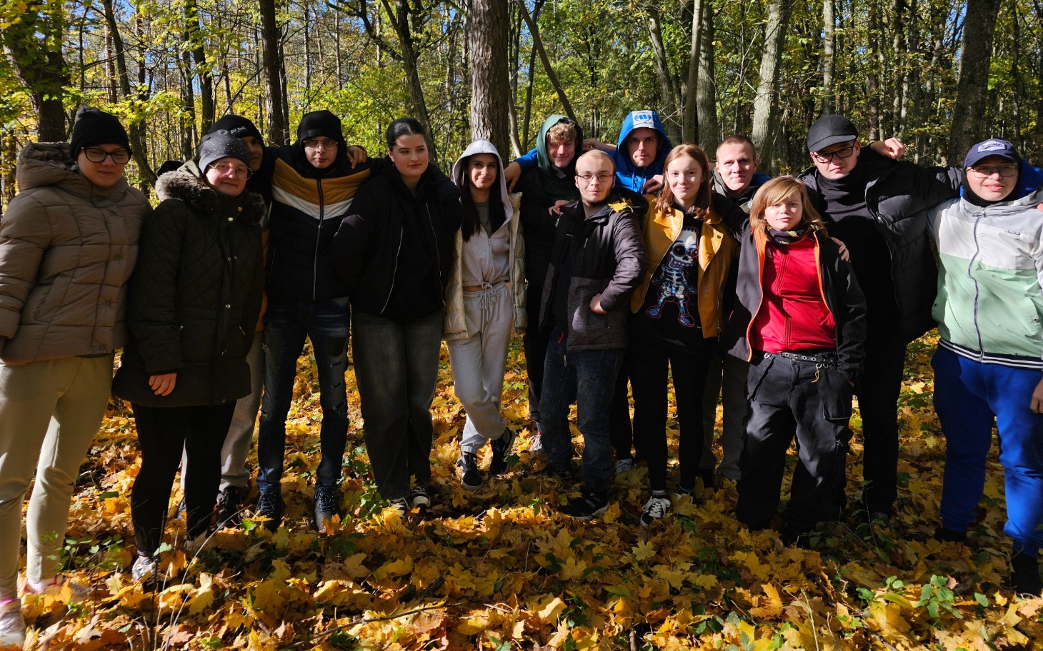 
        Grupa ludzi pozujących w lesie wśród opadłych liści.
    