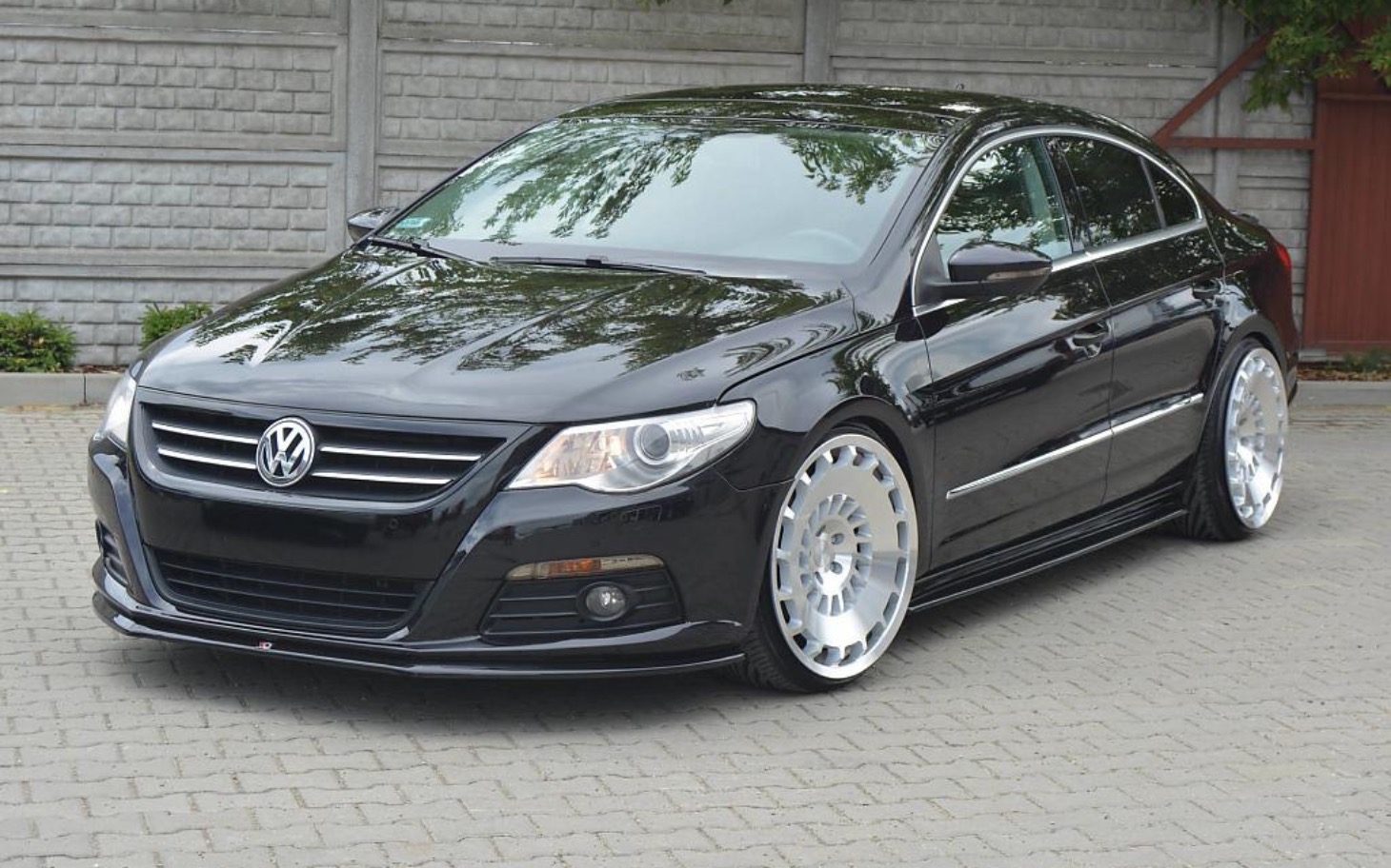 
        Czarny samochód Volkswagen z dużymi felgami na parkingu.
    