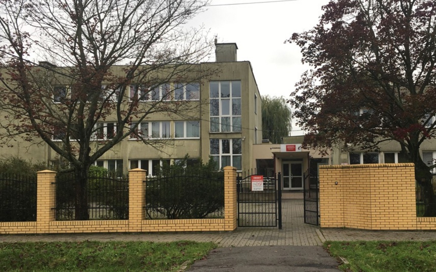 
        Budynek z ogrodzeniem, widok na wejście do instytucji.
    