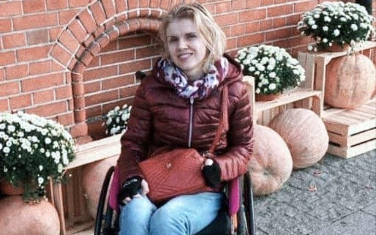 
        Kobieta na wózku inwalidzkim w otoczeniu dyni i kwiatów.
    