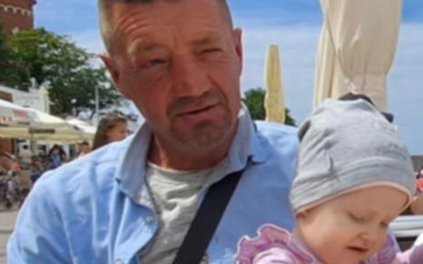 Mężczyzna z dzieckiem na rękach, w letnim otoczeniu.