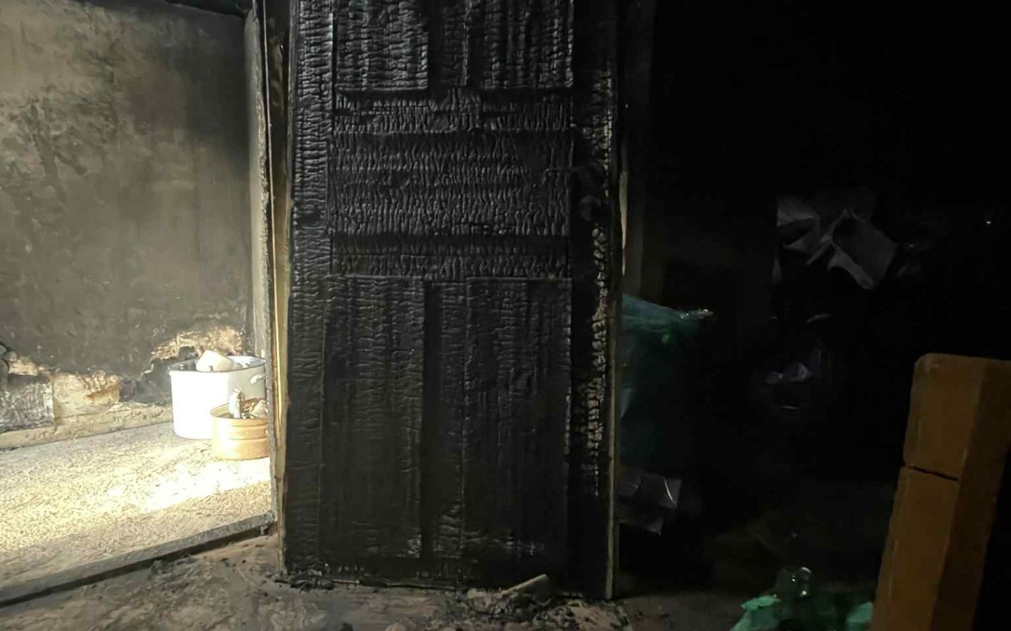 
        Zniszczone drzwi po pożarze, z czarnym popiołem.
    