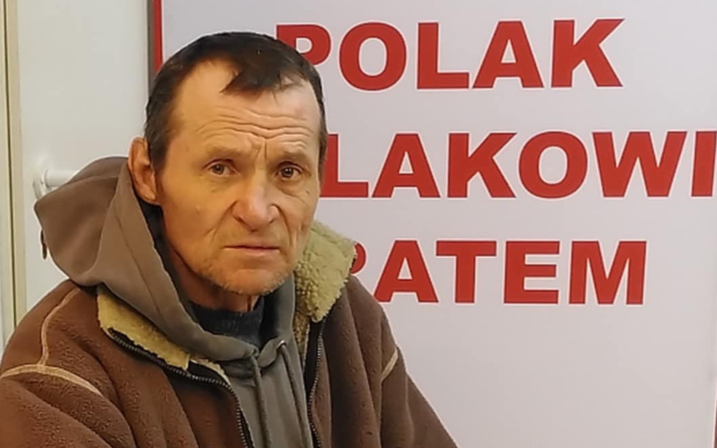 
        Mężczyzna siedzi przed dużym napisem, wyrażającym patriotyzm.
    