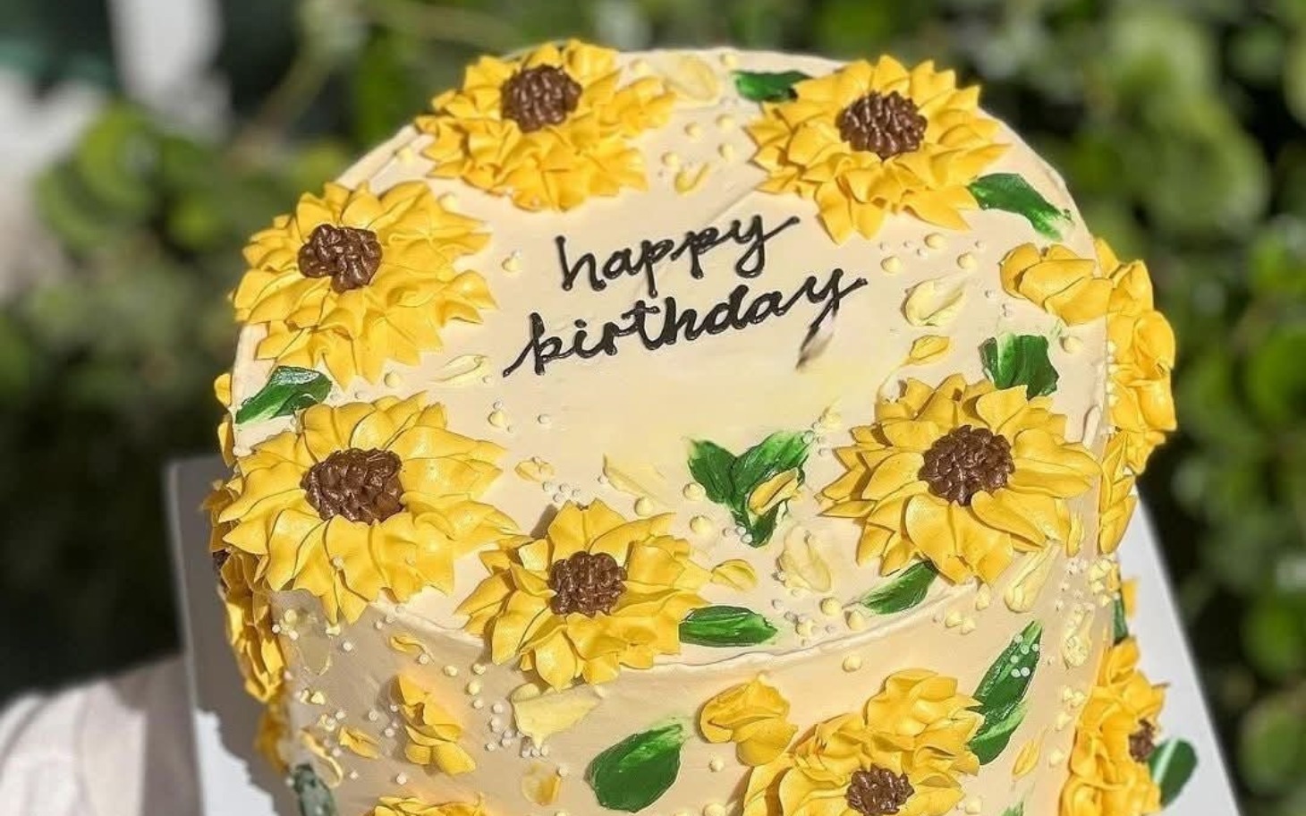 
        Tort urodzinowy ozdobiony słonecznikami z napisem 'happy birthday'.
    