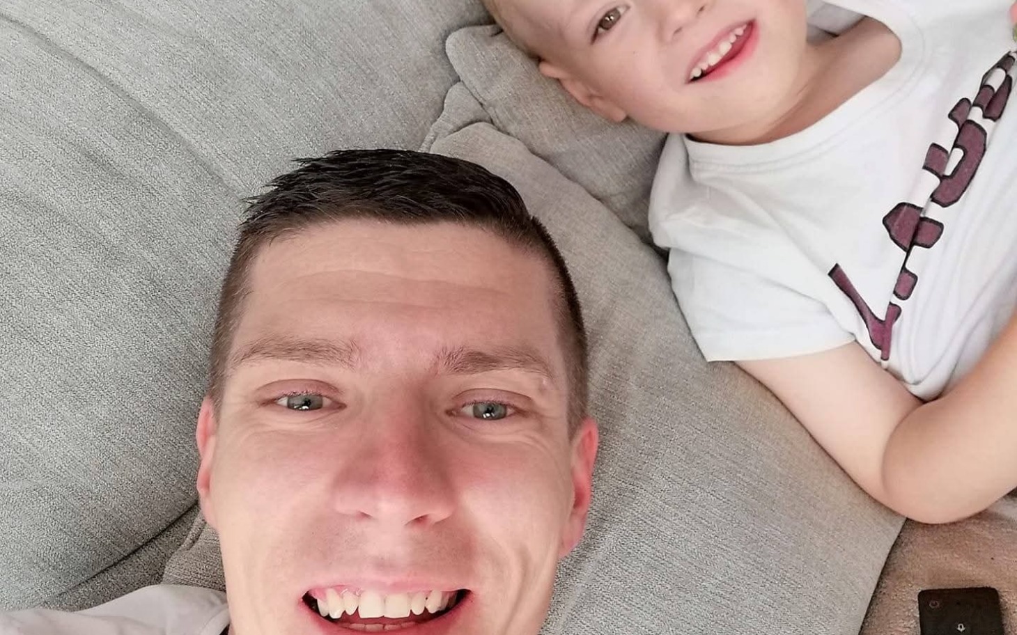 
        Mężczyzna z dzieckiem, obaj uśmiechnięci na kanapie.
    