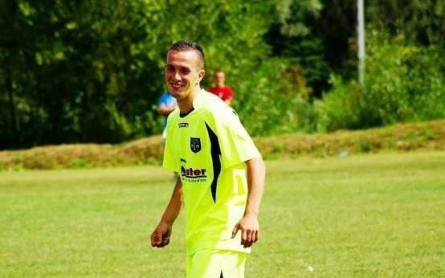 
        Mężczyzna w jaskrawym stroju piłkarskim, uśmiechający się na boisku.
    