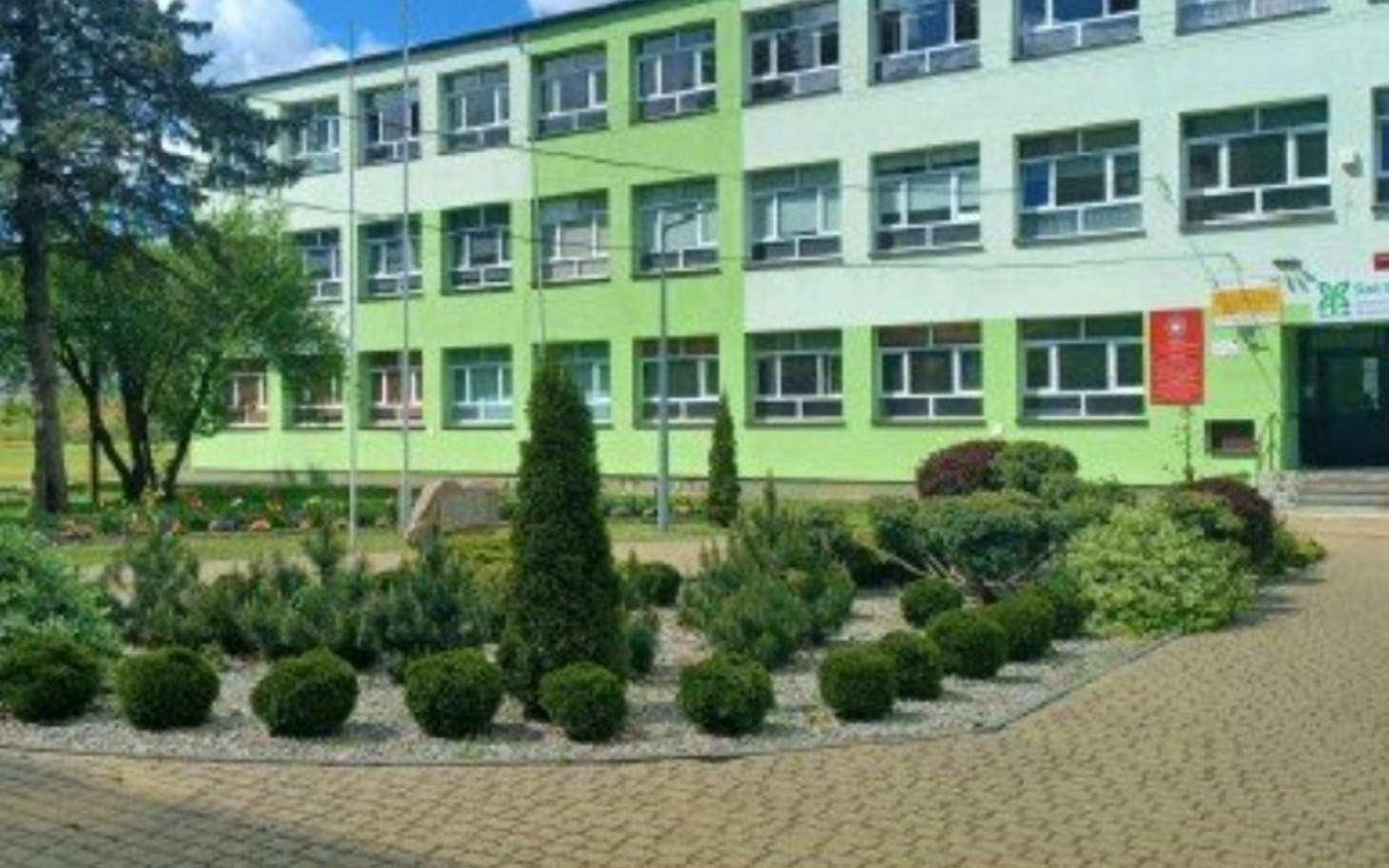 
        Budynek szkoły z zielonymi ścianami i ogrodem.
    