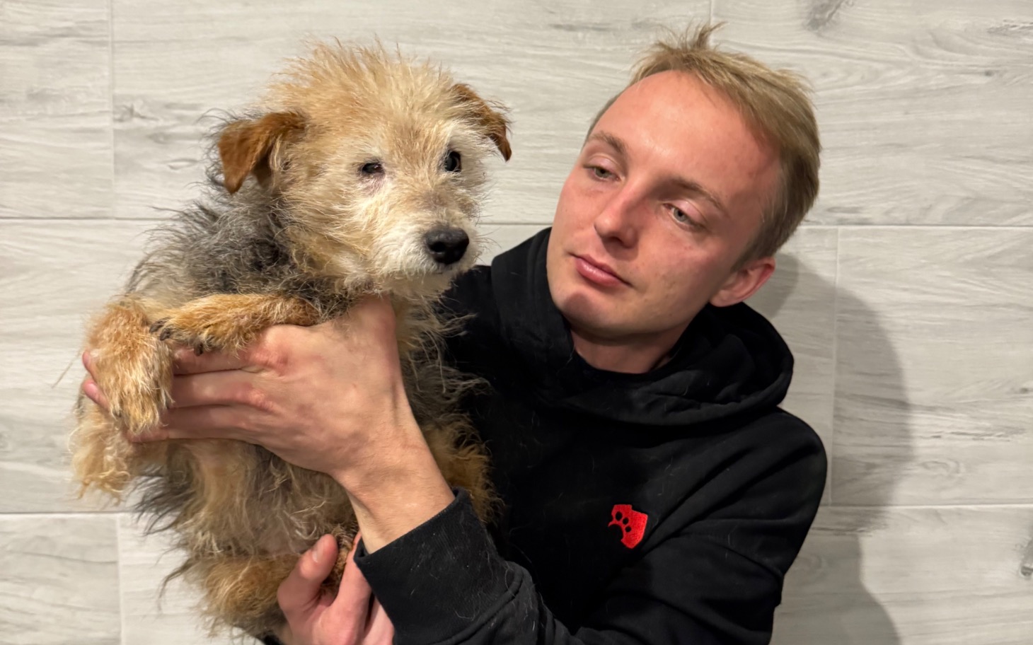 
        Młody mężczyzna trzyma psa w ramionach.
    