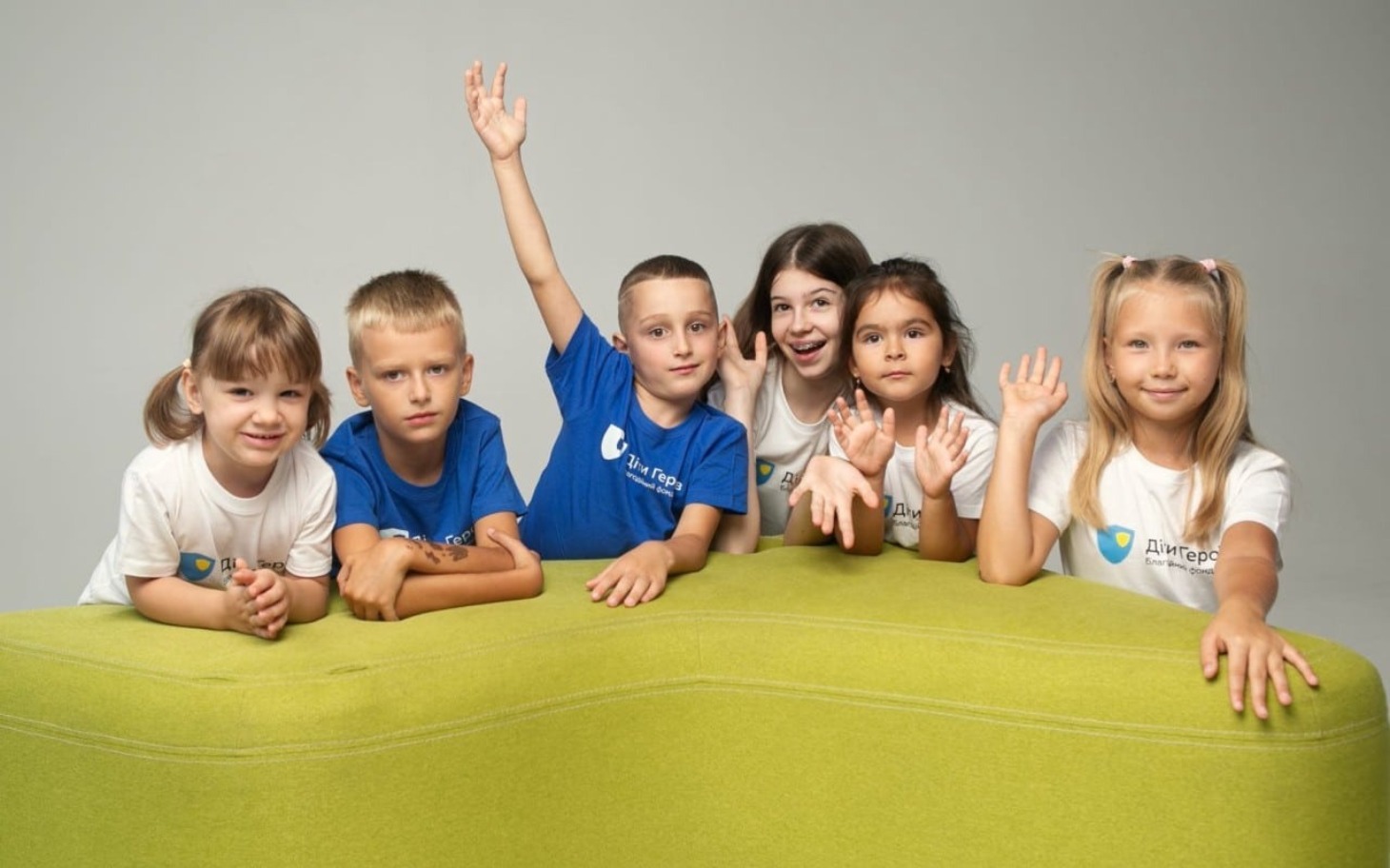 
        Grupa dzieci machających rękami, uśmiechniętych na kanapie.
    