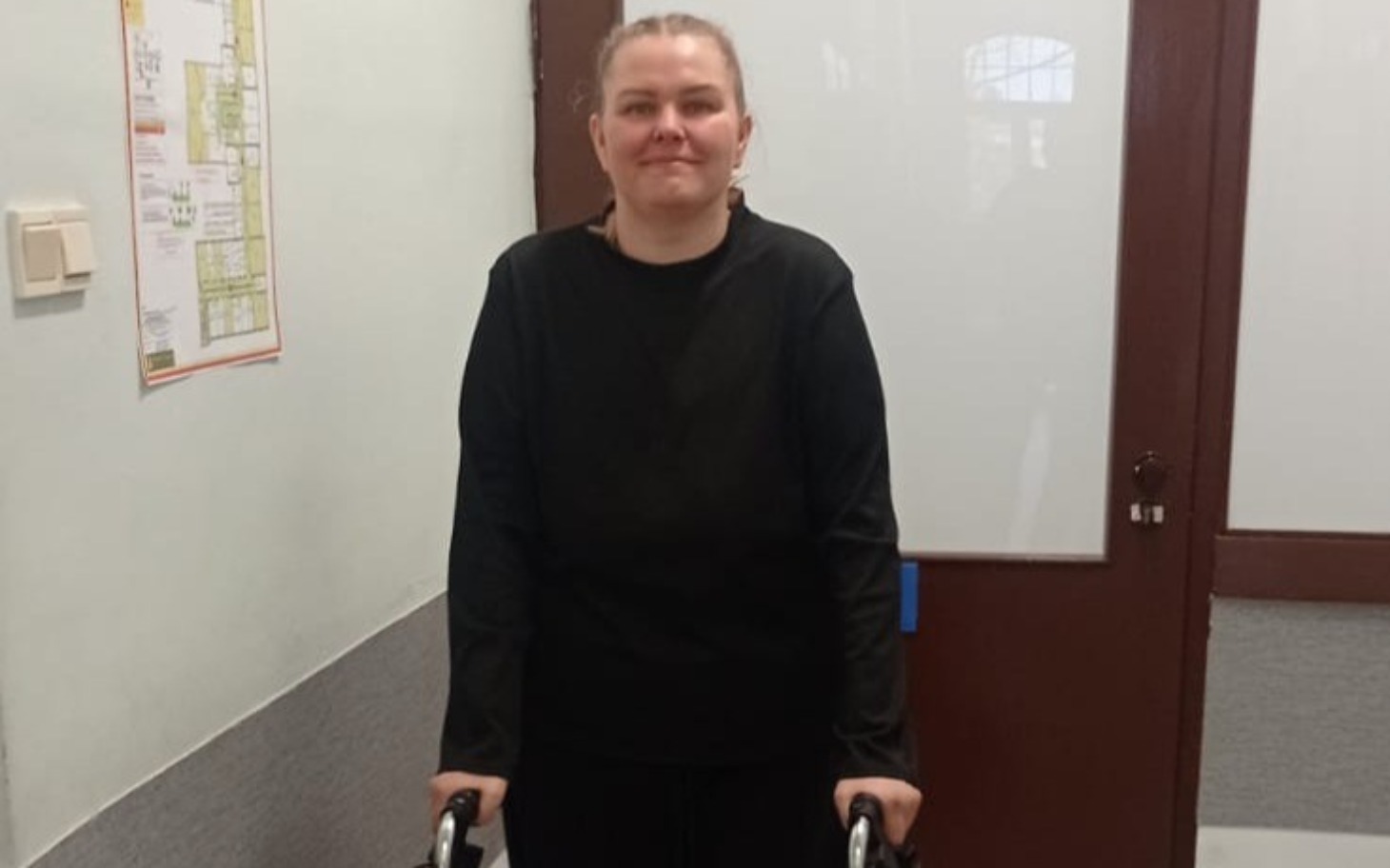 
        Młoda kobieta stoi z chodzikiem w korytarzu.
    