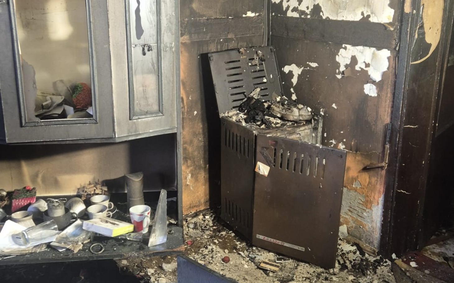 
        Zniszczona kuchnia po pożarze, z uszkodzonym piecem.
    