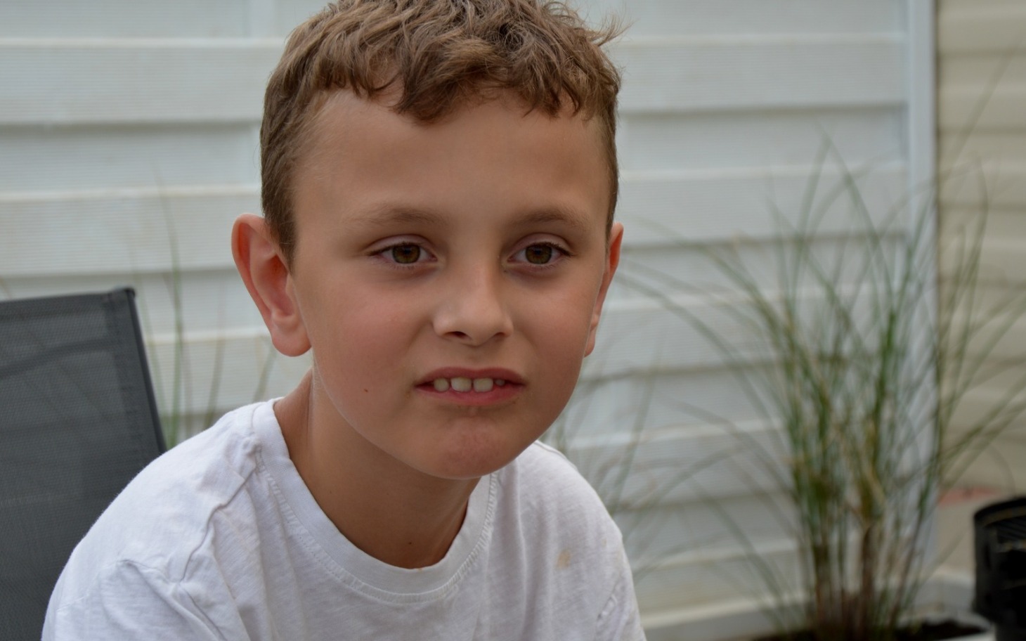 
        Chłopiec w białej koszulce, z zamyśloną miną, siedzi na zewnątrz.
    