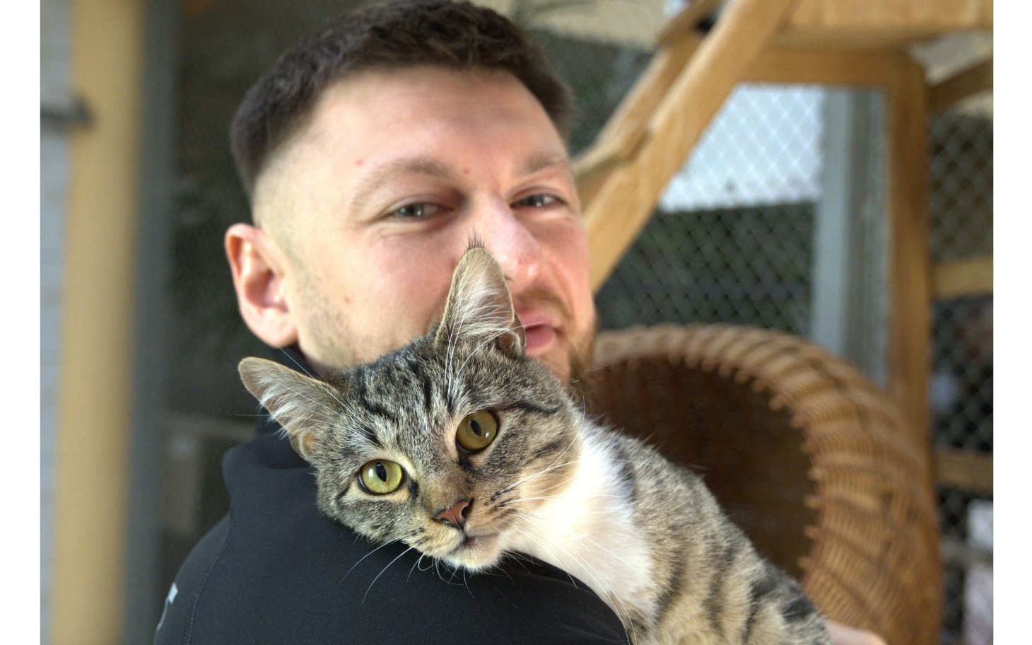 
        Mężczyzna trzyma kota na rękach, obaj uśmiechnięci.
    