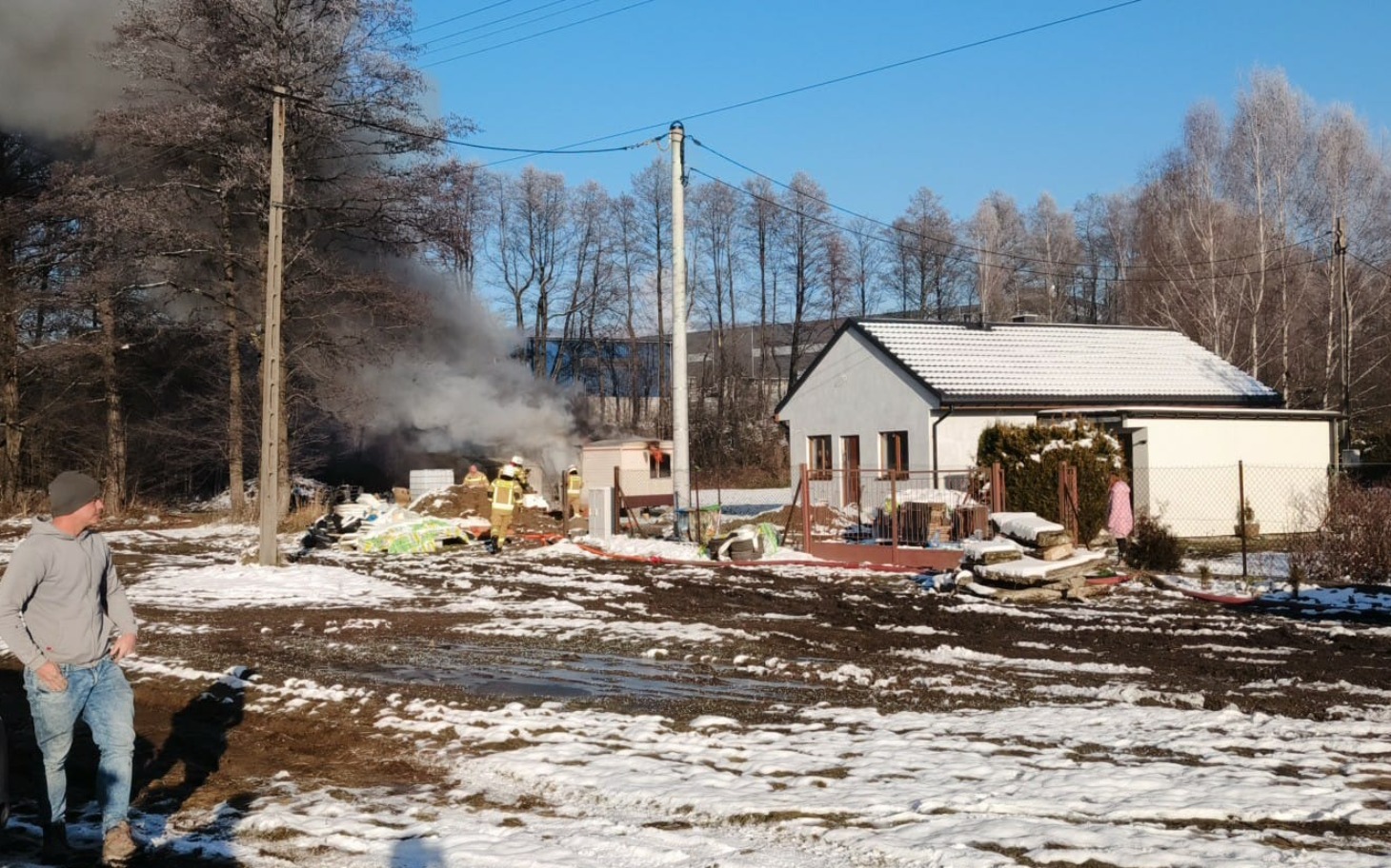 
        Pożar w pobliżu domu, dym unosi się w powietrzu.
    