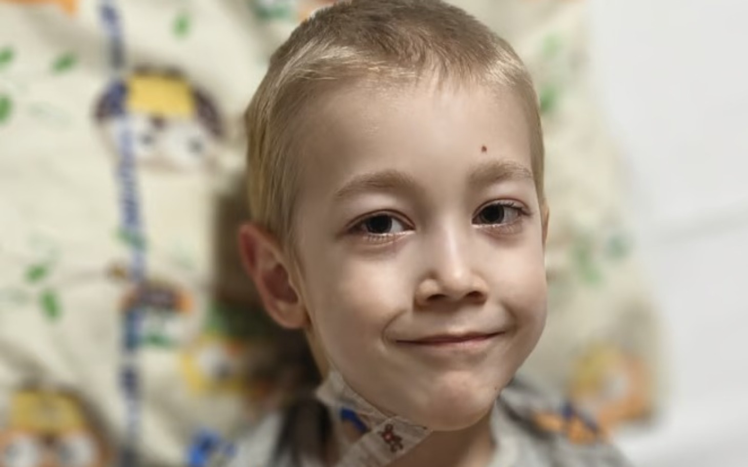 
        Chłopiec uśmiechający się w szpitalnym łóżku, z opatrunkiem na szyi.
    