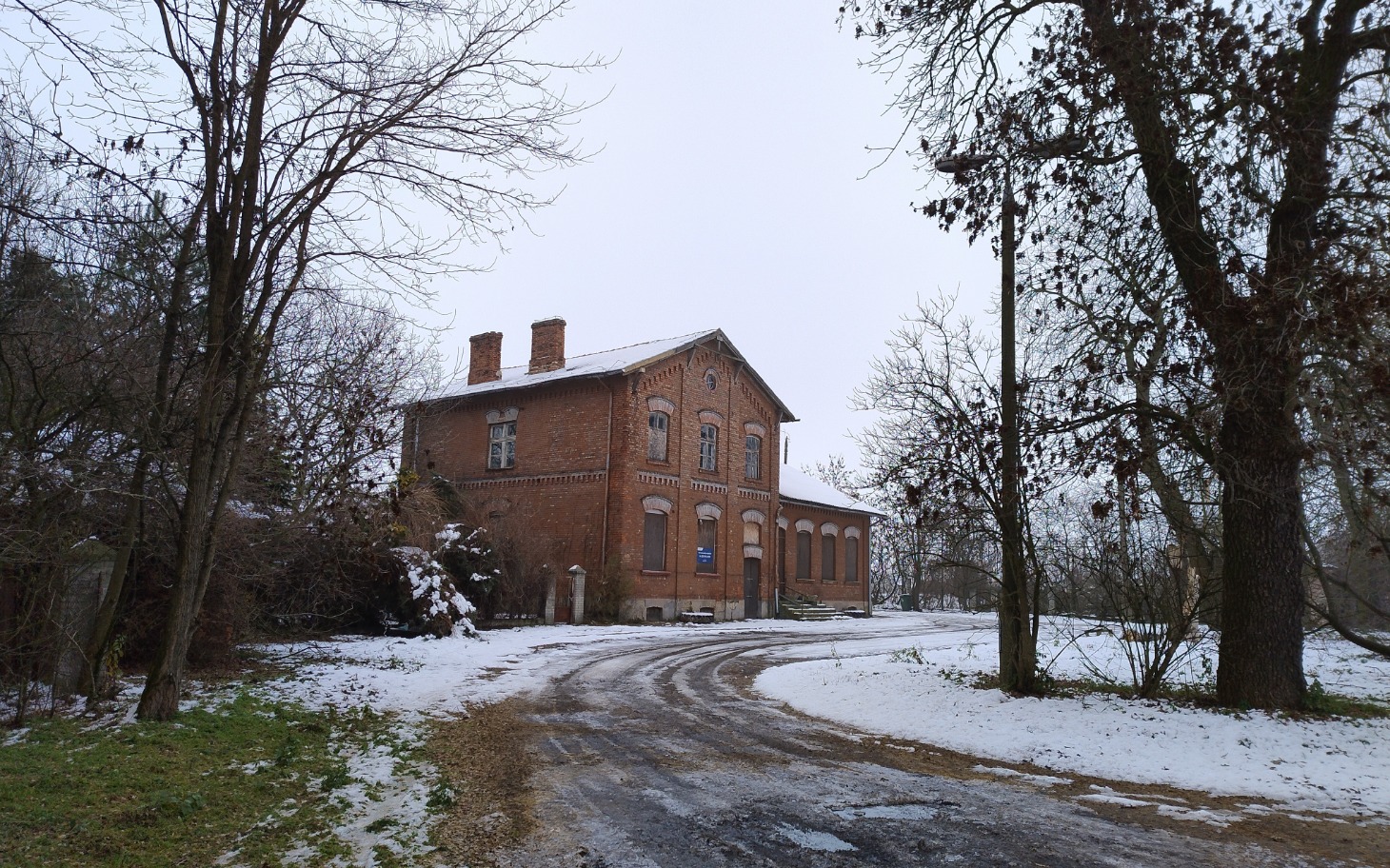 
        Stary budynek w zimowym krajobrazie, otoczony drzewami.
    