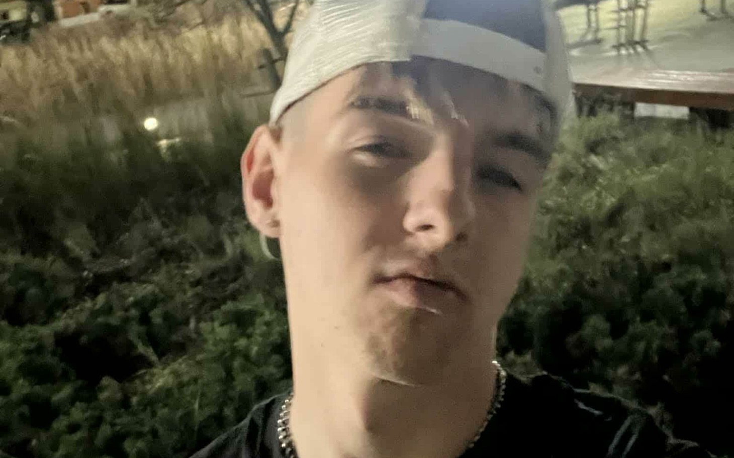 
        Młody mężczyzna w czapce, pozujący na tle zieleni.
    