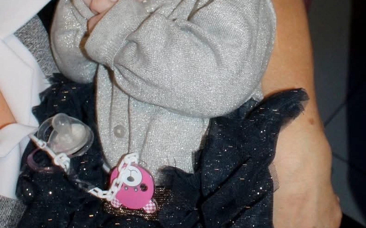 
        Mała dziewczynka w eleganckim stroju, trzymająca smoczek.
    