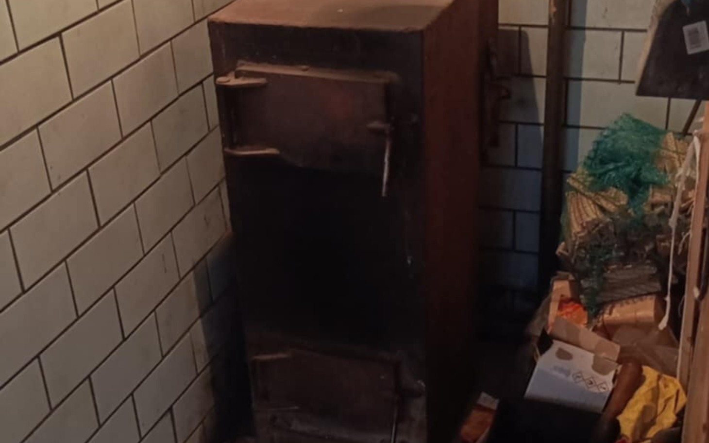 
        Stary piec w piwnicy, otoczony różnymi przedmiotami.
    