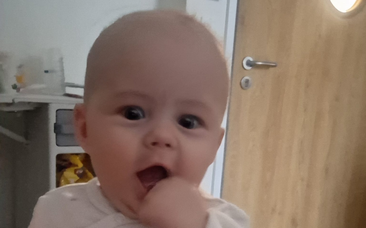 
        Uśmiechnięte niemowlę z ząbkami, trzymające palec w buzi.
    