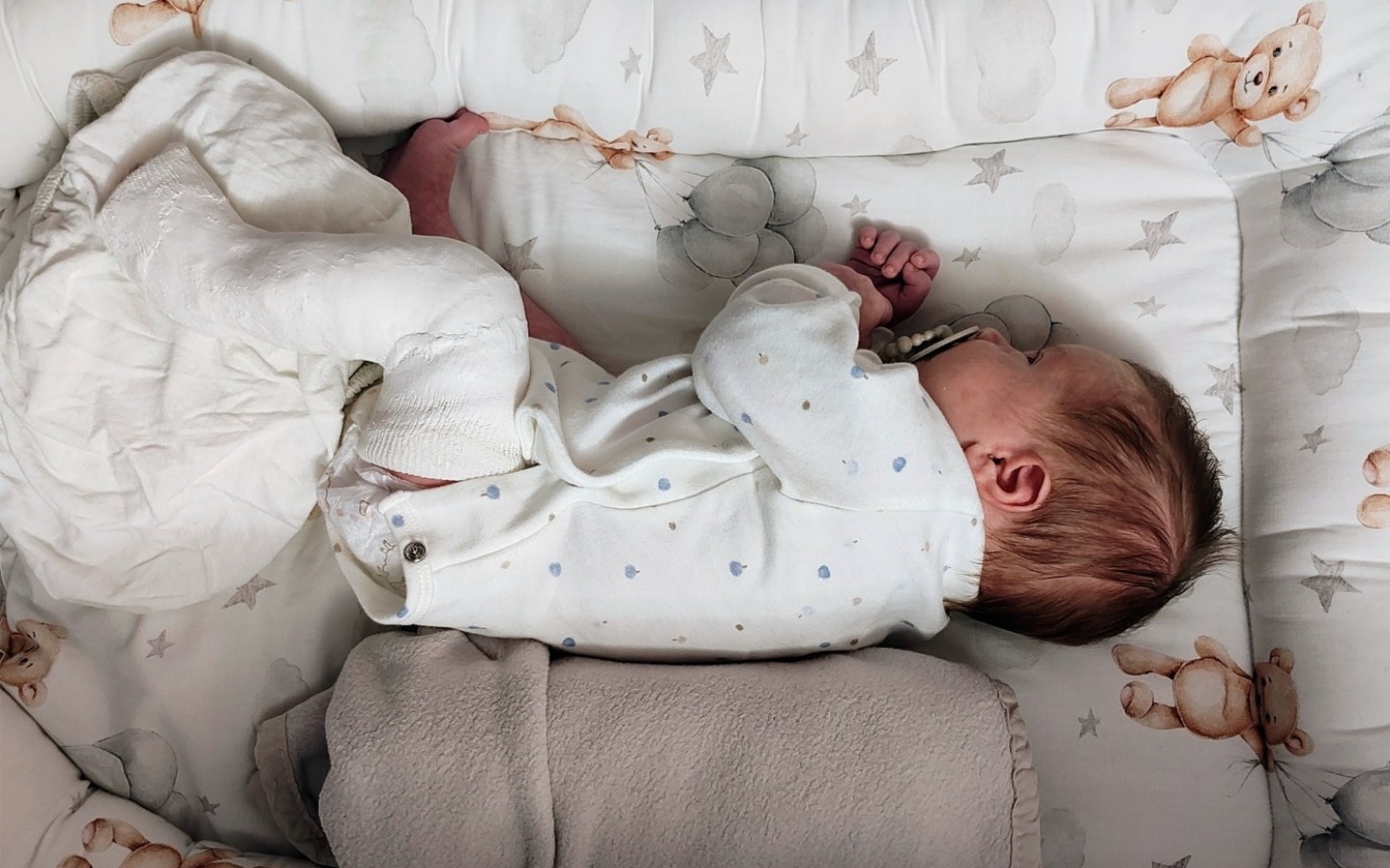
        Noworodek śpiący w łóżeczku, w otoczeniu kocyków.
    