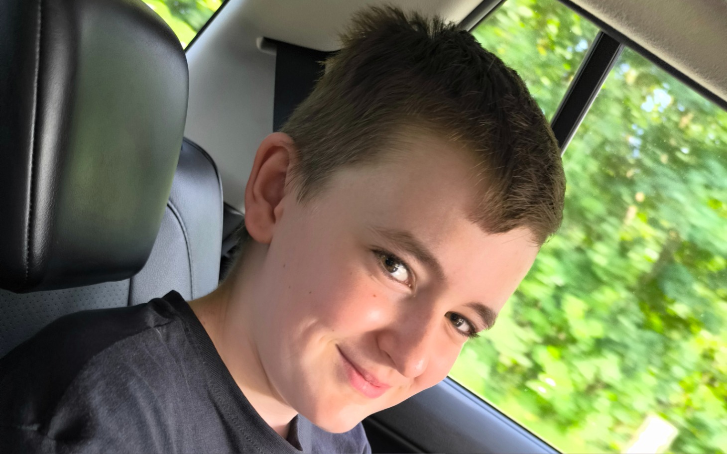 
        Chłopiec uśmiechający się w samochodzie, z zielonym tłem.
    