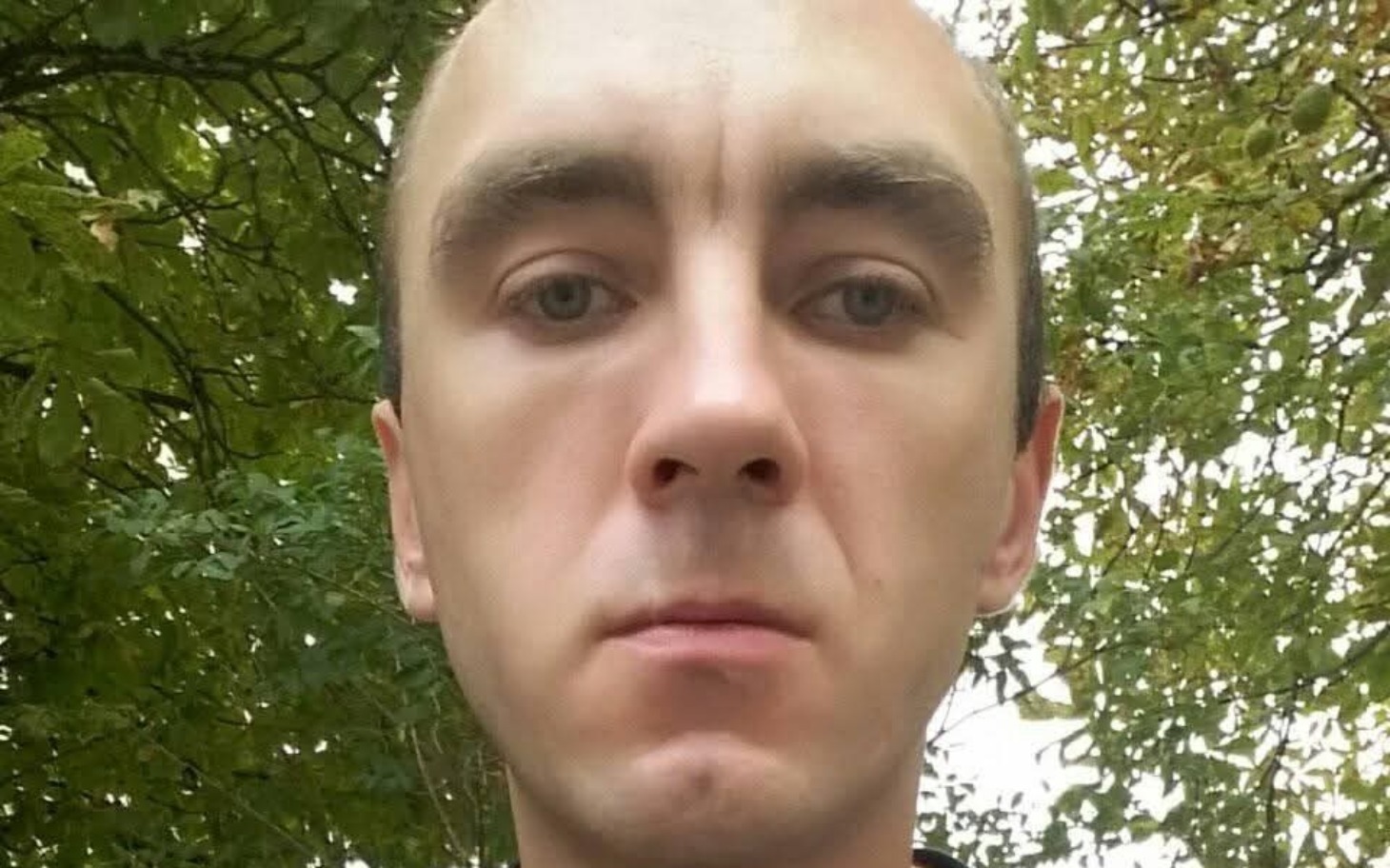 
        Mężczyzna na tle zieleni, z poważnym wyrazem twarzy.
    