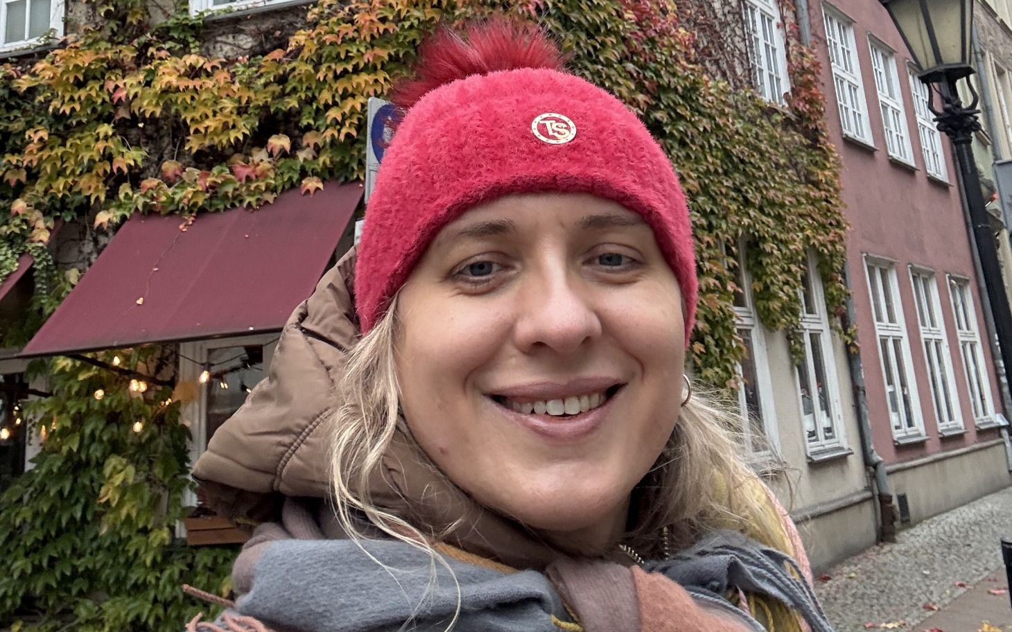 
        Uśmiechnięta kobieta w czerwonej czapce na tle kolorowych liści.
    