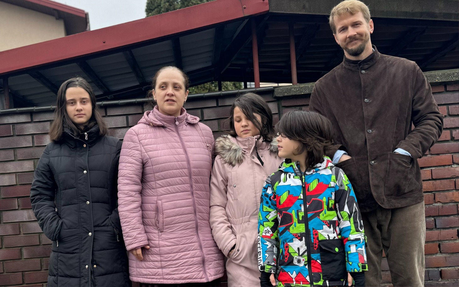 
        Rodzina pozująca na tle ogrodzenia.
    