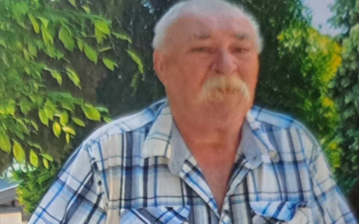 
        Starszy mężczyzna w koszuli w kratę, uśmiechający się w plenerze.
    