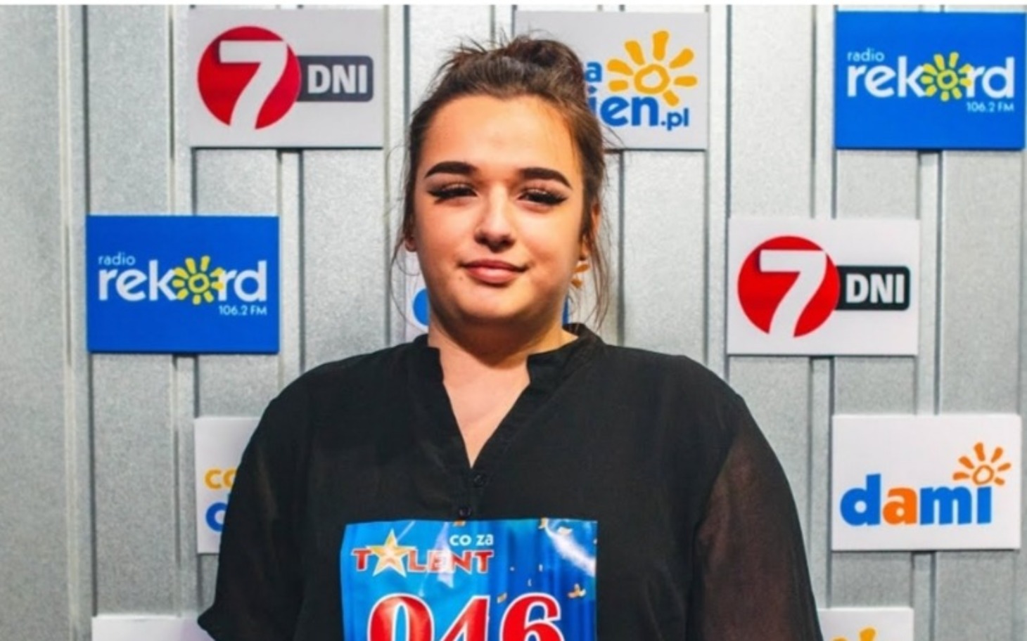 
        Młoda kobieta na scenie, trzymająca numer w konkursie talentów.
    