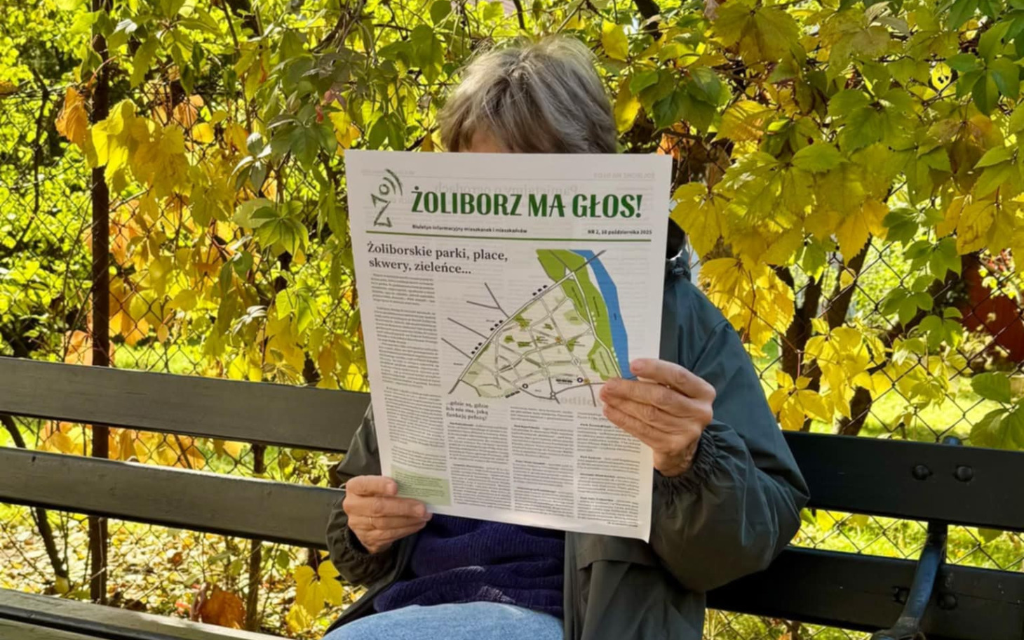 
        Osoba czytająca gazetę w parku, otoczona zielenią.
    