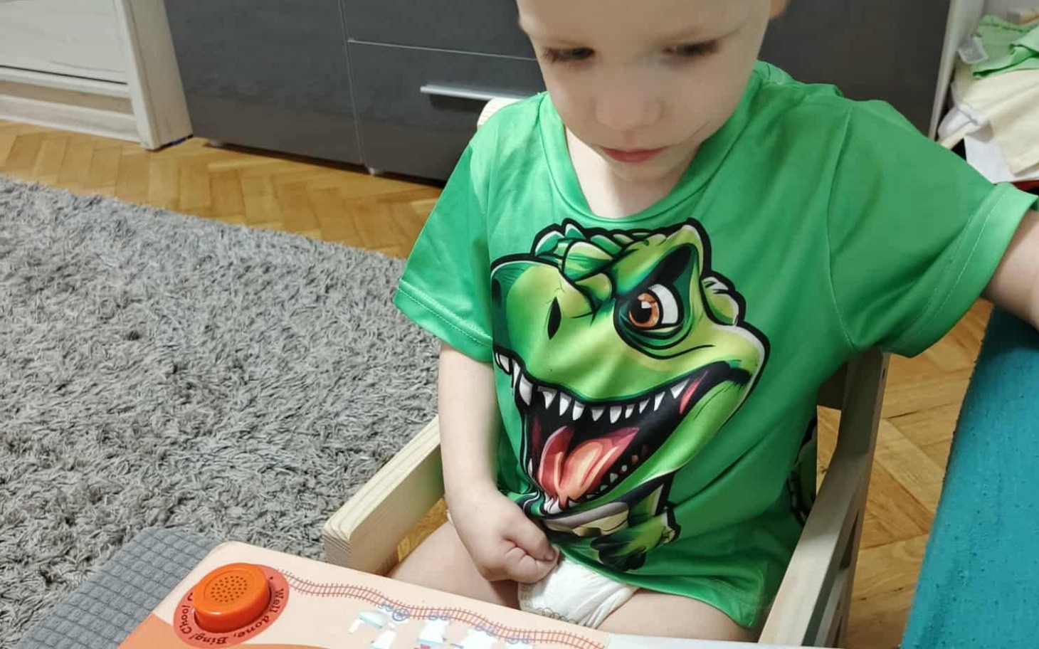 
        Chłopiec w zielonej koszulce z dinozaurem bawi się zabawką.
    