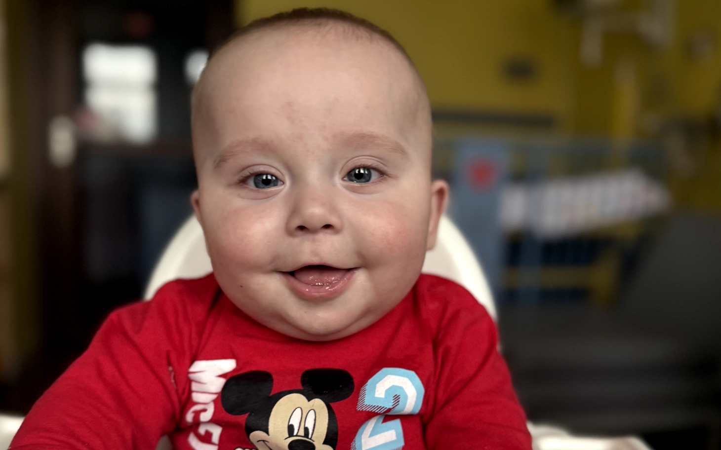 
        Uśmiechnięty niemowlak w czerwonym body z Mikiem Mousem.
    