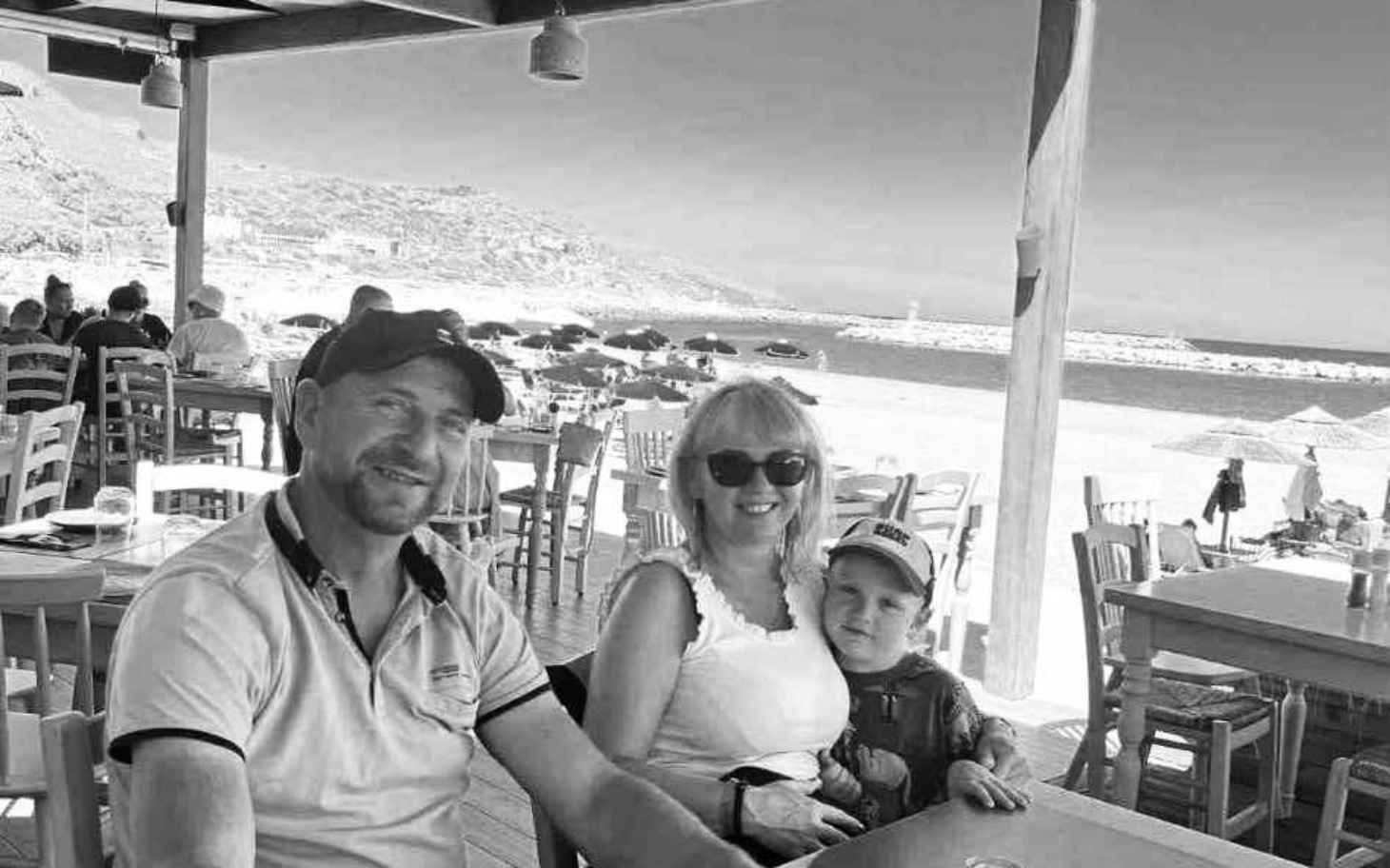 
        Rodzina na wakacjach, uśmiechnięta przy stole w restauracji.
    