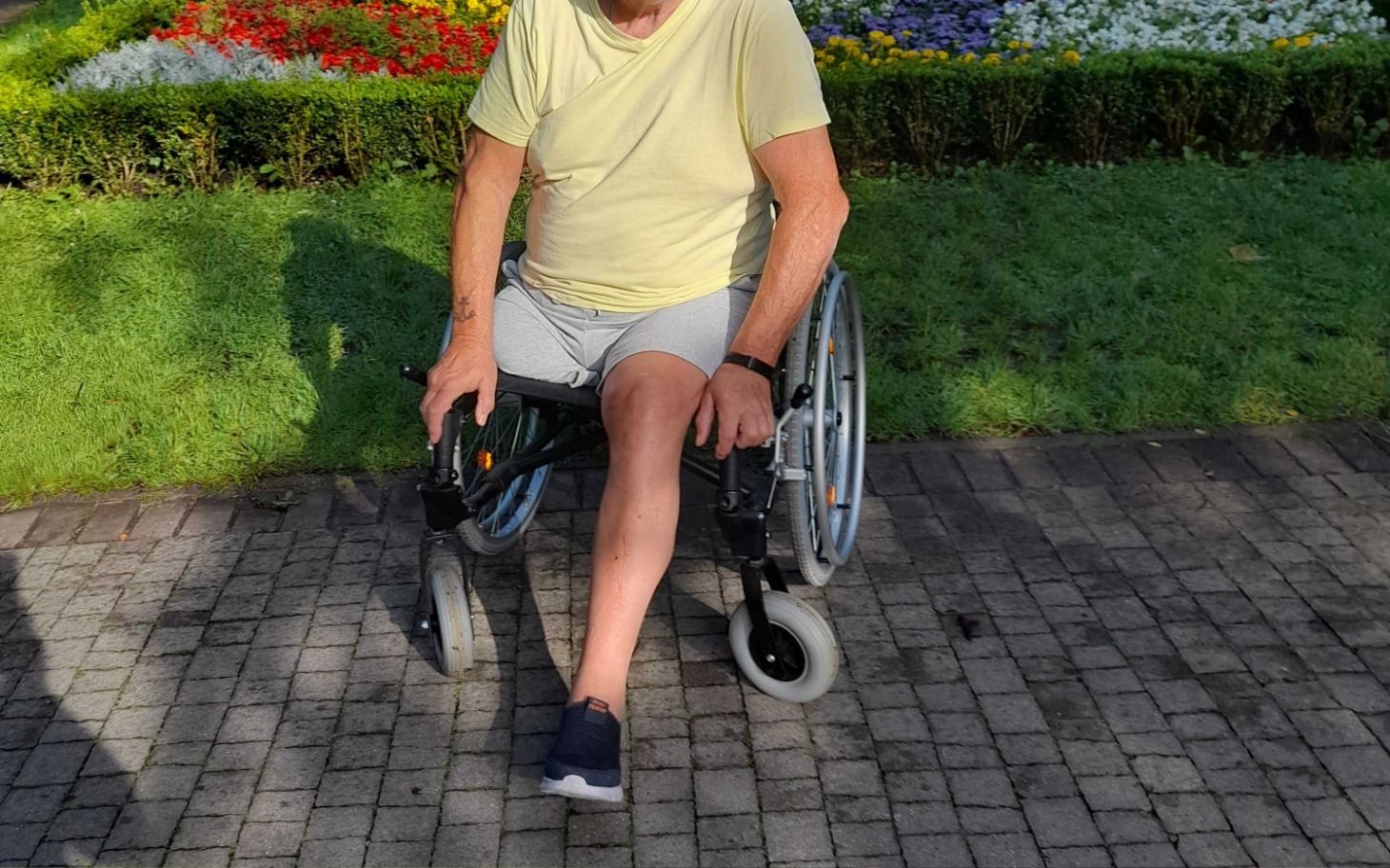
        Mężczyzna w żółtej koszulce siedzący na wózku inwalidzkim w parku.
    