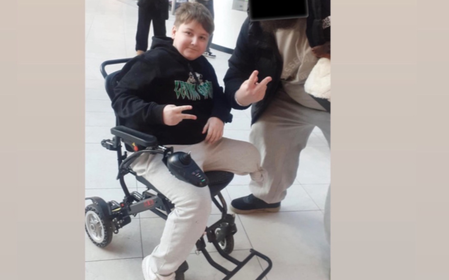 
        Chłopiec na wóku inwalidzkim w kadrze, uśmiech i gesty pokazujące radość.
    