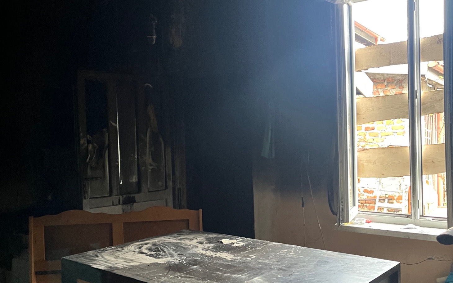 
        Ciemne wnętrze z popalonym stołem i oknem wpuszczającym światło.
    