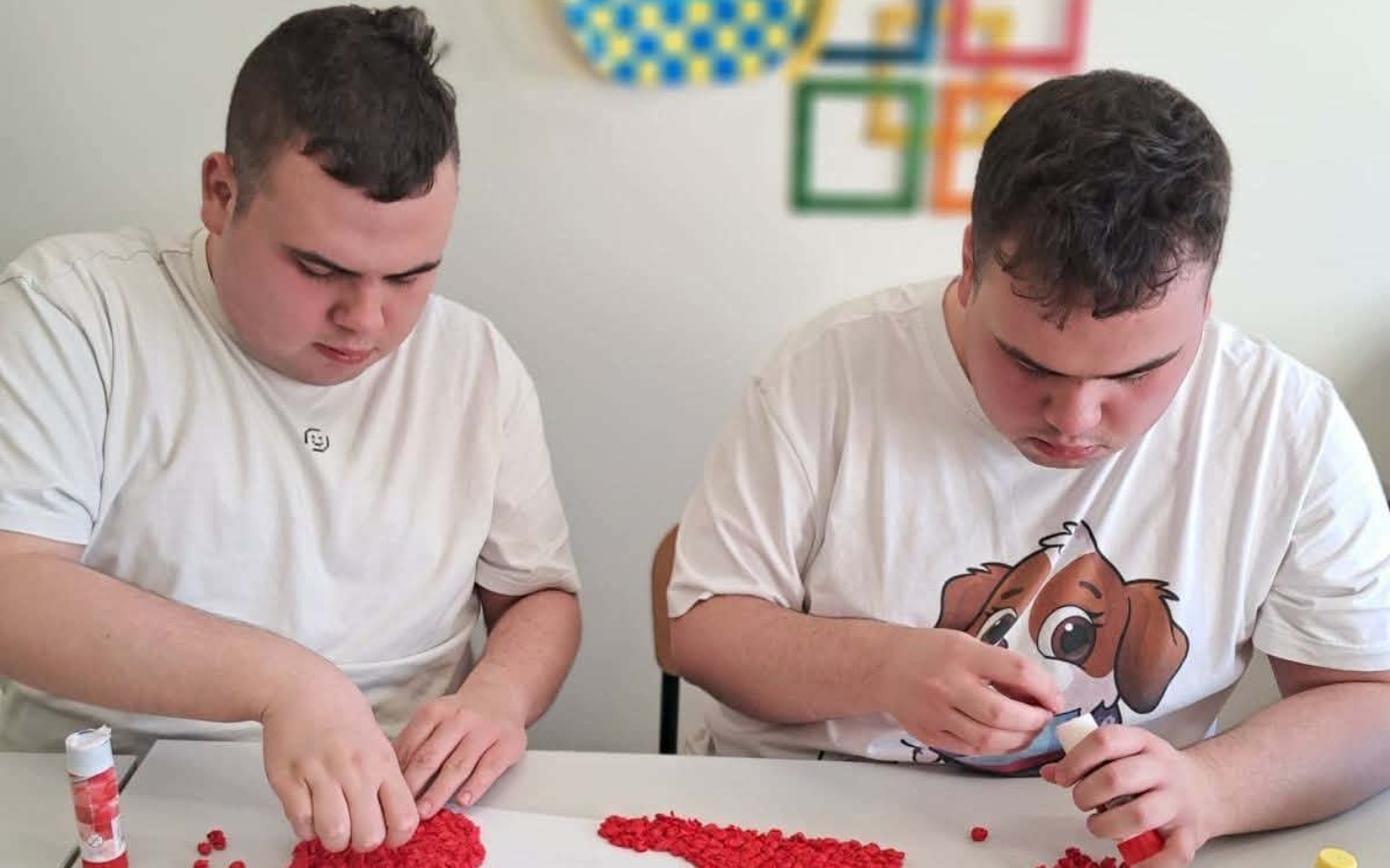 
        Dwaj chłopcy pracujący nad kreatywnym projektem z czerwonymi elementami.
    