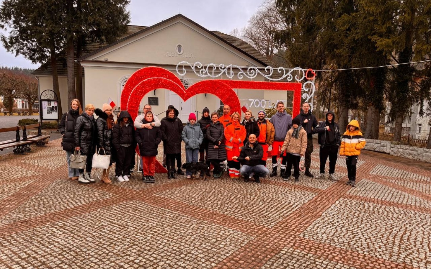 
        Grupa ludzi pozująca przed dużym sercem w parku.
    