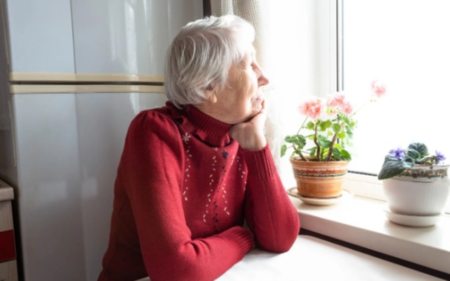 
        Starsza kobieta patrzy przez okno, myśląc o życiu.
    