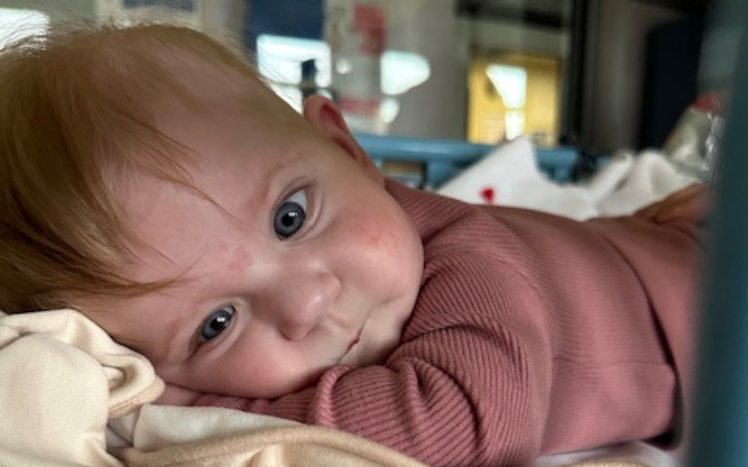 
        Małe dziecko leży na kocu, uśmiechając się do kamery.
    