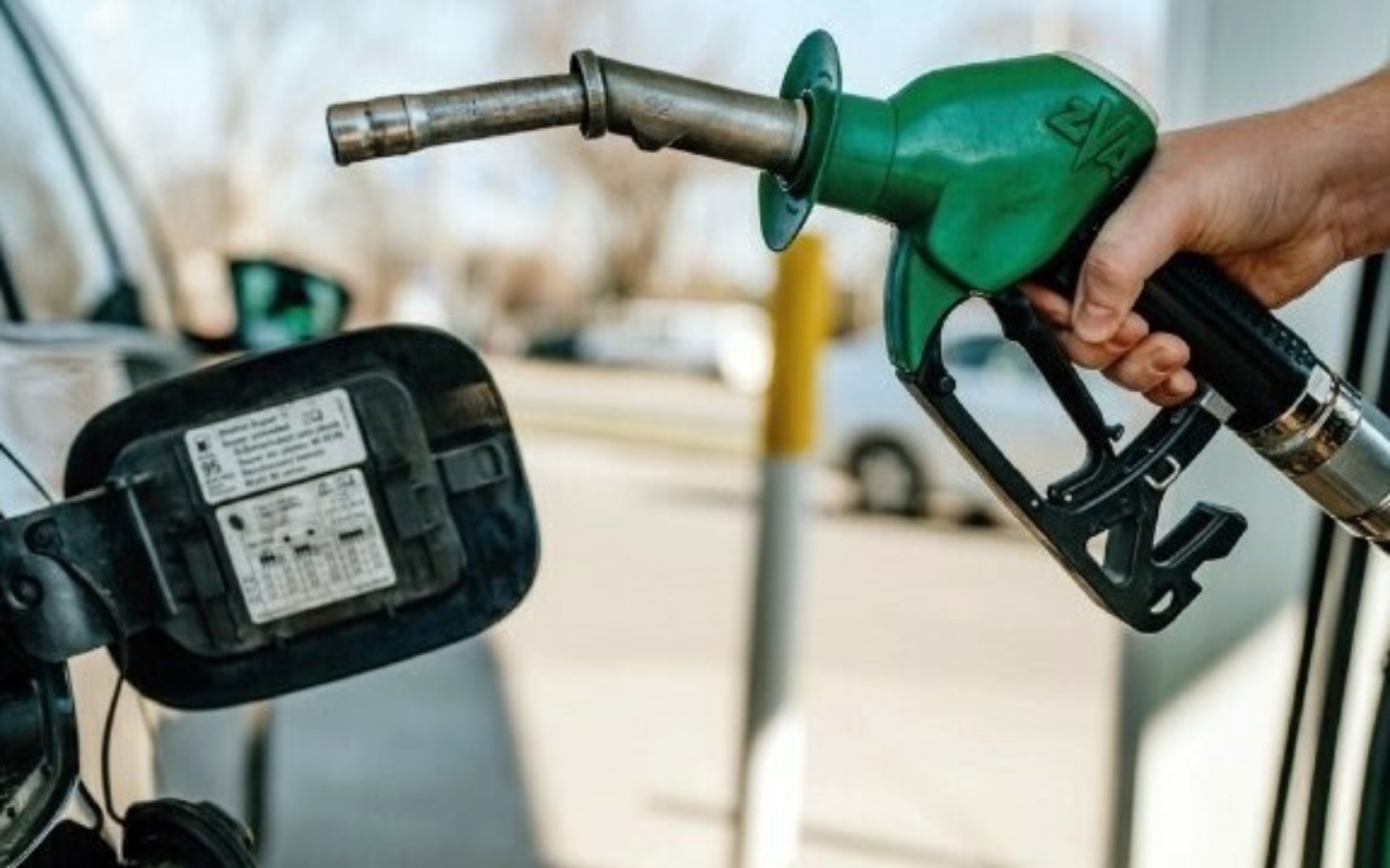 
        Osoba tankująca samochód zieloną pistoletem do paliwa.
    