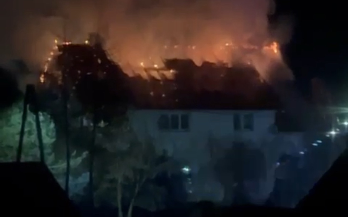 
        Płonący budynek w nocy, ogień wydobywa się z dachu.
    