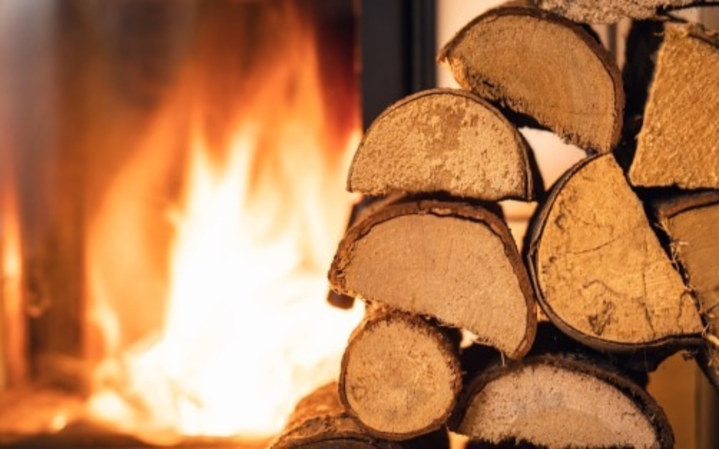 
        Stos drewna obok paleniska, w tle płonące ognisko.
    