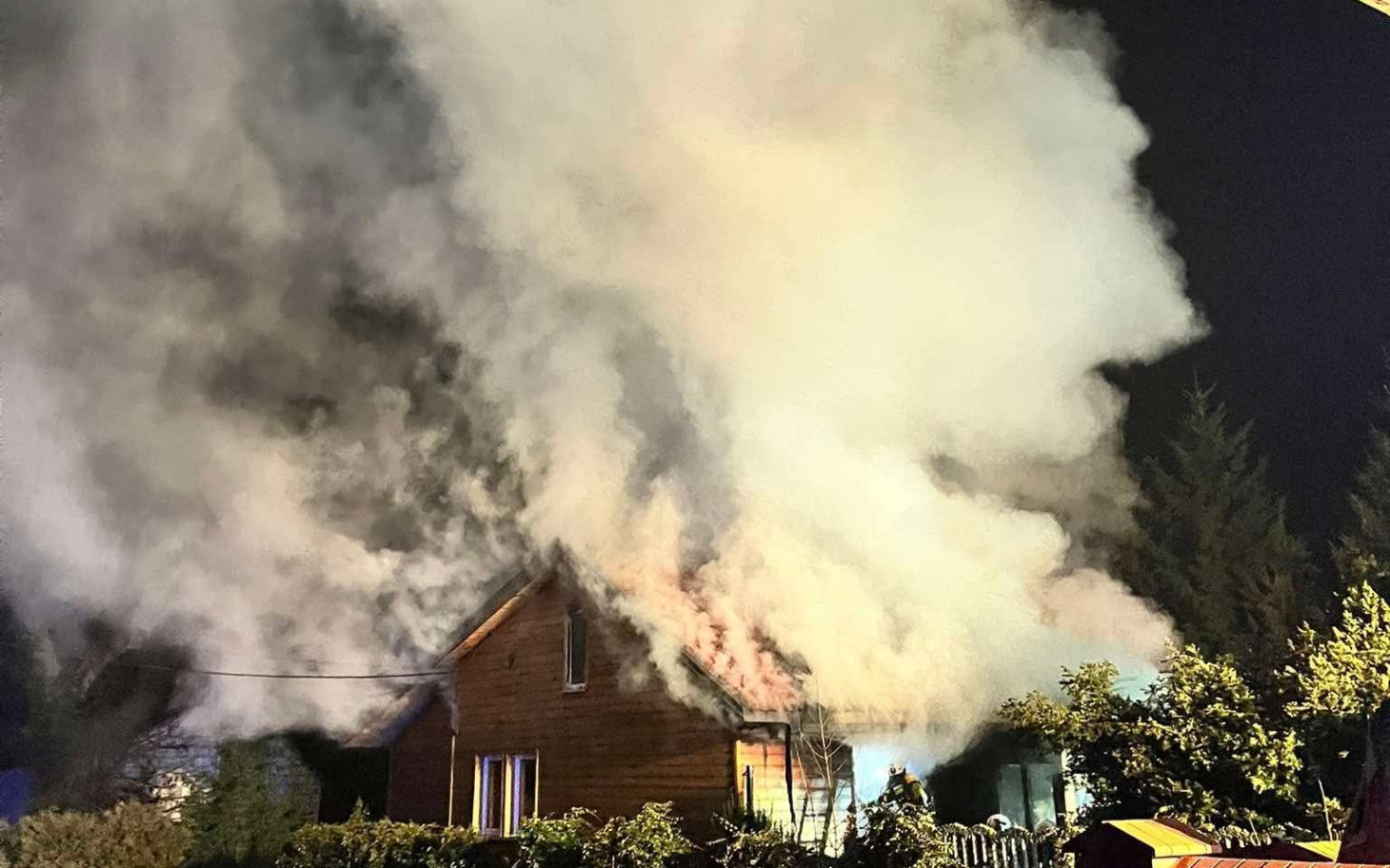 
        Dom w ogniu, z dużą ilością dymu unoszącego się w powietrzu.
    