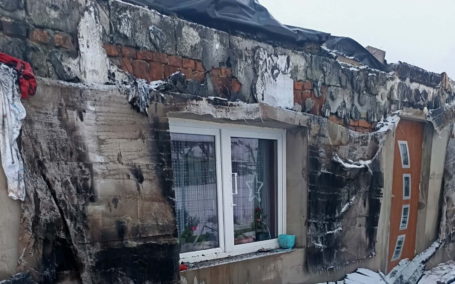 
        Zniszczona ściana budynku po pożarze, z widocznymi uszkodzeniami.
    