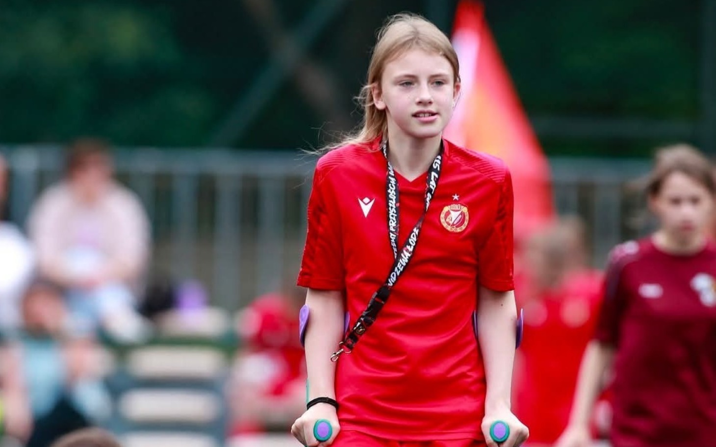 
        Młoda dziewczyna w czerwonym stroju sportowym, trzymająca sprzęt.
    