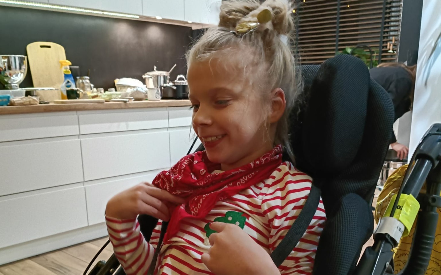 
        Uśmiechnięta dziewczynka w wózku, z chustą na szyi.
    