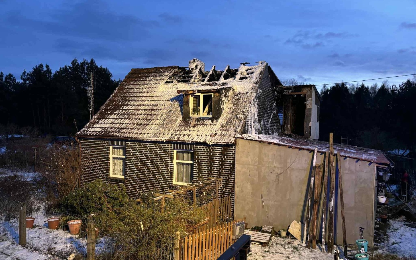 
        Zniszczony dom po pożarze, z uszkodzonym dachem i widocznymi śladami zniszczeń.
    